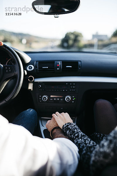Rückansicht der Hände eines Paares am Getriebe während der Autofahrt