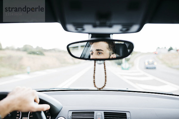 Junger Mann beim Autofahren  Nahaufnahme des Rückspiegels