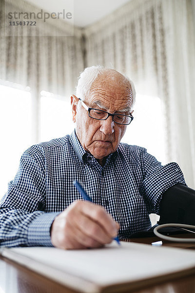 Ein älterer Mann  der seinen Blutdruck kontrolliert und das Ergebnis aufschreibt.