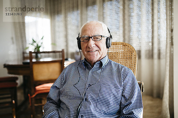 Porträt eines lächelnden älteren Mannes  der zu Hause Musik mit Kopfhörern hört.