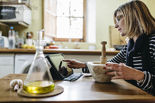 Frau mit digitaler Tablette bei der Zubereitung von Knoblauchmayonnaise in ihrer Küche