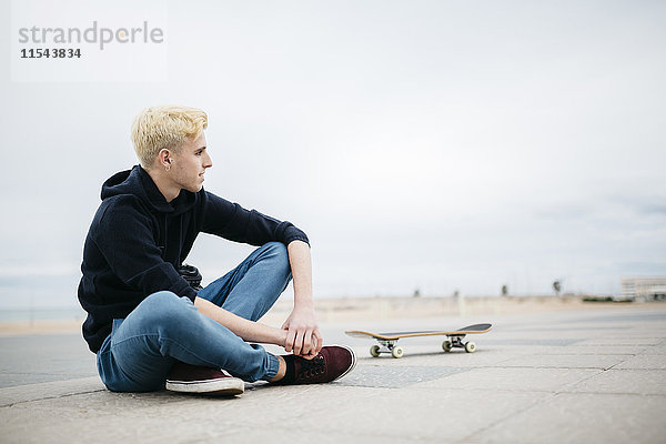 Spanien  Torredembarra  junger Skateboarder auf dem Boden sitzend  entspannend