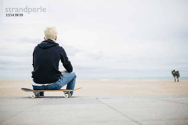 Spanien  Torredembarra  Rücken eines jungen Mannes auf seinem Skateboard mit Blick aufs Meer