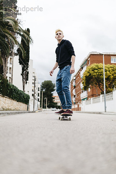 Spanien  Torredembarra  lächelnder junger Mann auf seinem Skateboard