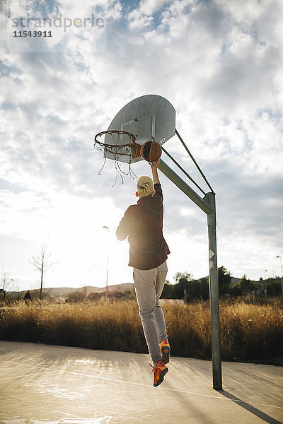 Junger Mann spielt Basketball auf einem Außenplatz