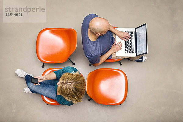 Mann und Frau sitzen auf Stühlen mit tragbaren Geräten