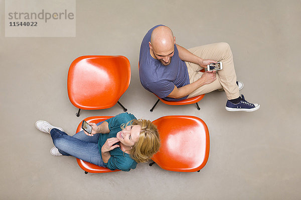 Mann und Frau sitzen auf Stühlen mit Smartphones