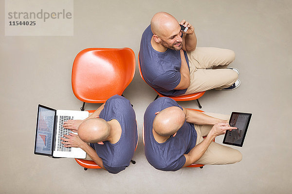 Mann sitzt auf Stühlen mit tragbaren Geräten  Multitasking