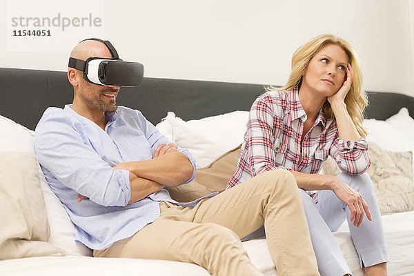 Mann mit Virtual Reality Brille sitzt auf der Couch neben seiner gelangweilten Frau