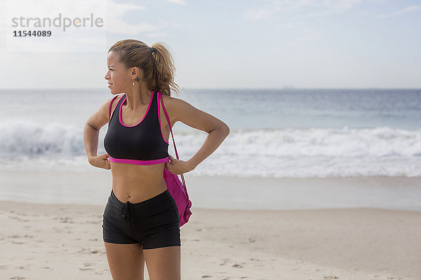 Sportliche Frau steht am Strand und schaut in die Ferne.