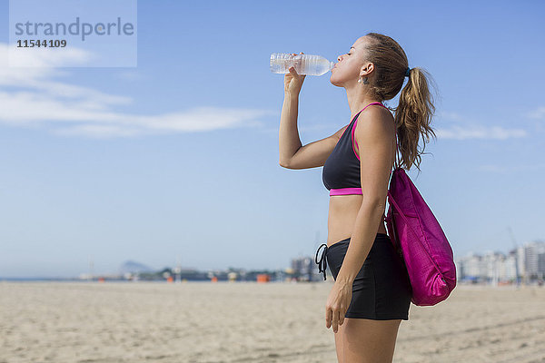 Brasilien  Rio de Janeiro  Copacabana  sportliche Frau mit Trinkwasser am Strand