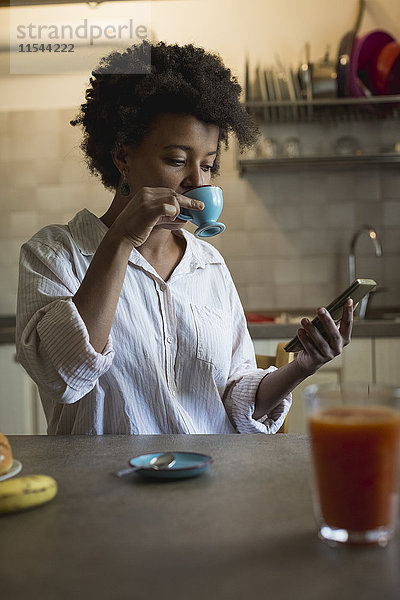 Porträt einer jungen Frau  die in ihrer Küche Espresso trinkt  während sie das Phablet betrachtet.