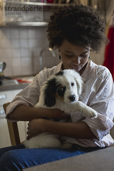Junge Frau sitzend mit Hund auf dem Schoß in der Küche