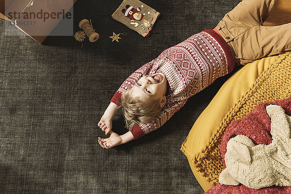 Kleiner Junge lacht und spielt auf dem Teppich mit einer Schachtel Weihnachtsdekoration