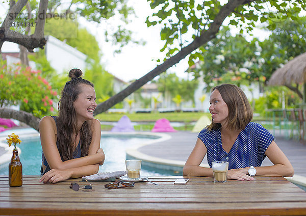 Zwei glückliche Frauen  die am Tisch am Pool sitzen und reden.