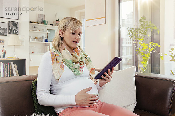 Schwangere Frau mit digitalem Tablett zu Hause