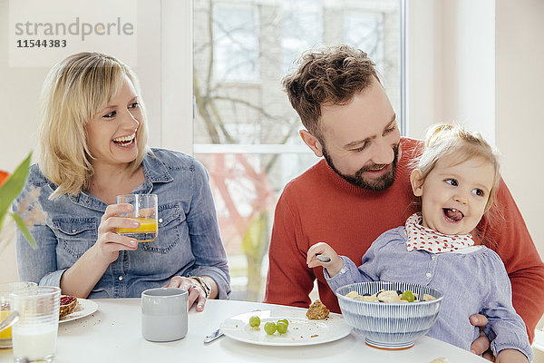 Kleines Mädchen isst Müsli mit Früchten am Frühstückstisch