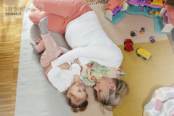 Schwangere Mutter und kleine Tochter beim Kuscheln auf dem Teppich zu Hause