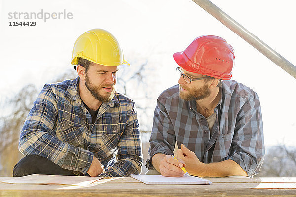 Zwei Handwerker diskutieren und notieren auf der Baustelle