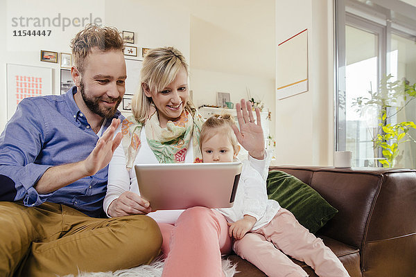 Eltern und kleine Tochter skyping mit digitalem Tablett zu Hause