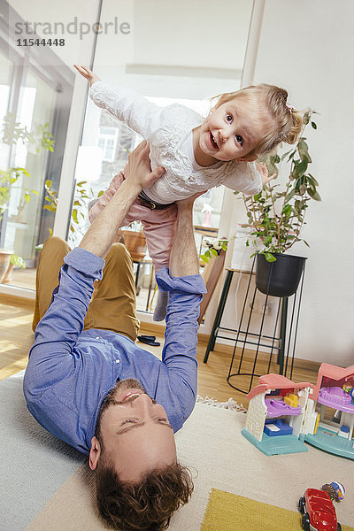 Mann liegt auf dem Boden und spielt mit seiner kleinen Tochter.