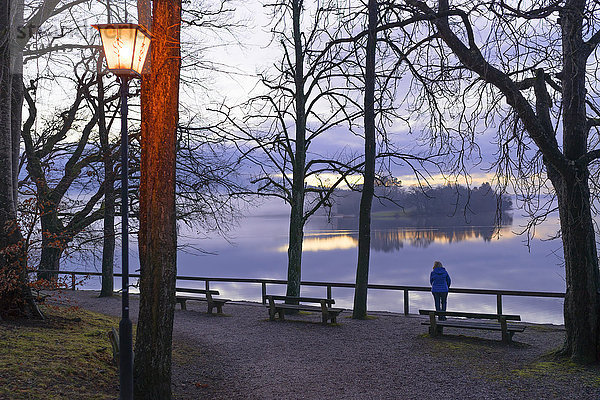 Deutschland  Bayern  Staffelsee  Seniorin am Seeufer bei Dämmerung