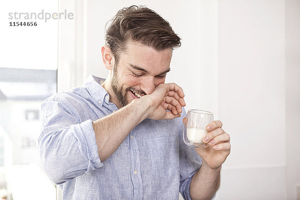 Lachender junger Mann mit einem Glas Milch  der sich den Mund wischt.