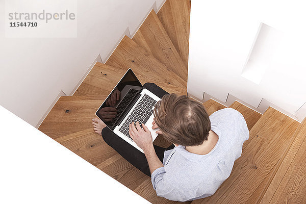 Mann auf Holztreppe sitzend mit Laptop