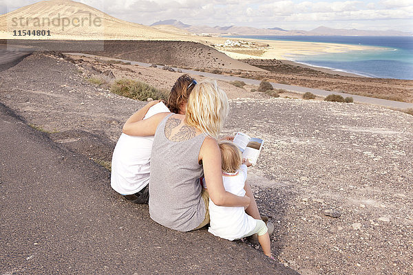 Spanien  Fuerteventura  Jandia  Familie an der Küste sitzend mit Blick in den Reiseführer