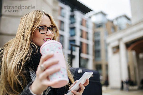 Lächelnde junge Frau mit Kaffee zum Mitnehmen und Handy im Freien