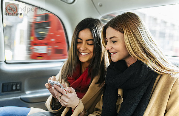 UK  London  Zwei junge Frauen mit Smartphone in schwarzer Kabine