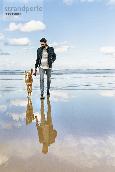 Mann  der mit seinem Hund am Strand spazieren geht.