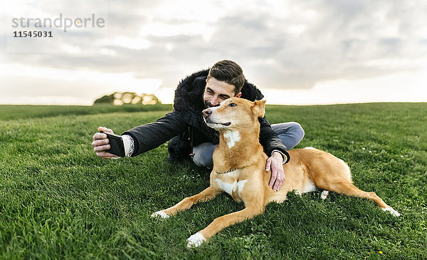 Mann  der einen Selfie mit seinem Hund auf einer Wiese nimmt.