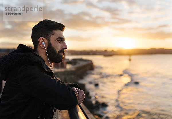 Spanien  Gijon  bärtiger Mann beim Musikhören mit Kopfhörern bei Sonnenuntergang