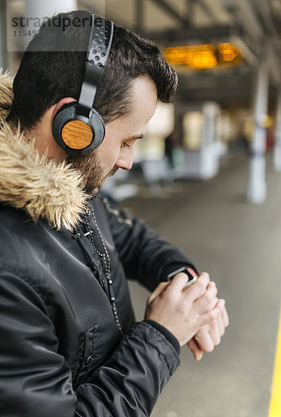 Mann mit Kopfhörer auf Plattform stehend mit smartwatch