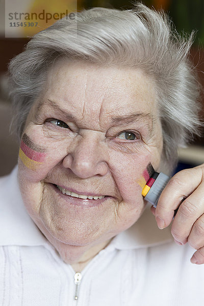 Porträt einer selbstbewussten Seniorin  die deutsche Nationalfarben auf die Wange malt.