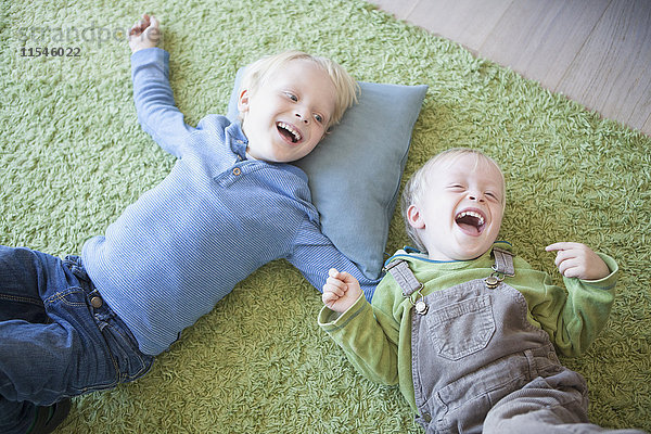 zwei lachende kleine Brüder  die zu Hause auf dem grünen Teppich liegen.
