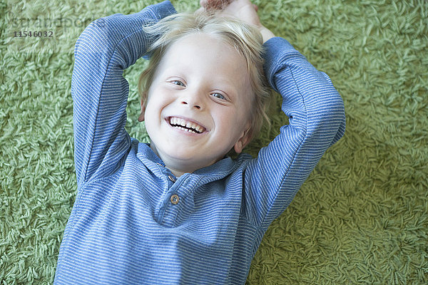 Porträt eines fröhlichen kleinen blonden Jungen auf grünem Teppich liegend