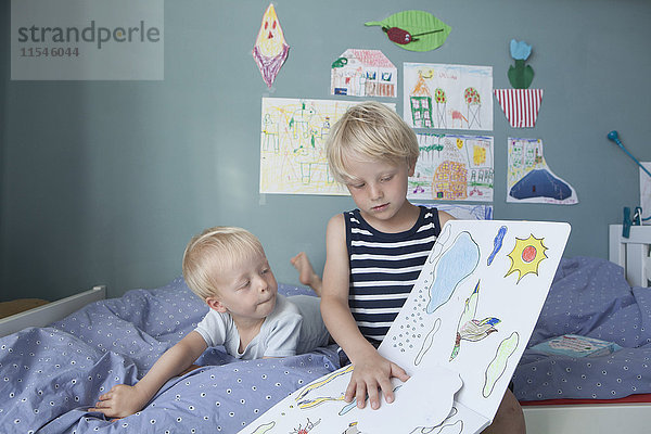 Zwei kleine Brüder auf dem Bett im Kinderzimmer beim Betrachten des Bilderbuches