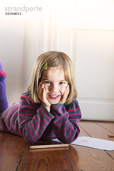 Porträt eines kleinen Mädchens auf dem Boden liegend mit Papier und Buntstiften