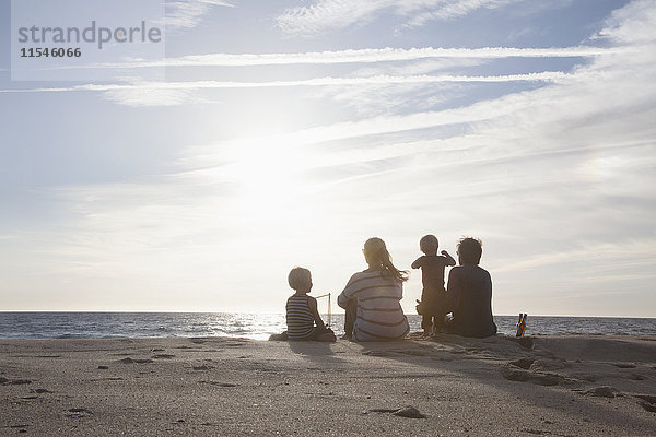 Rückansicht der Familie mit zwei Kindern am Strand bei Dämmerung