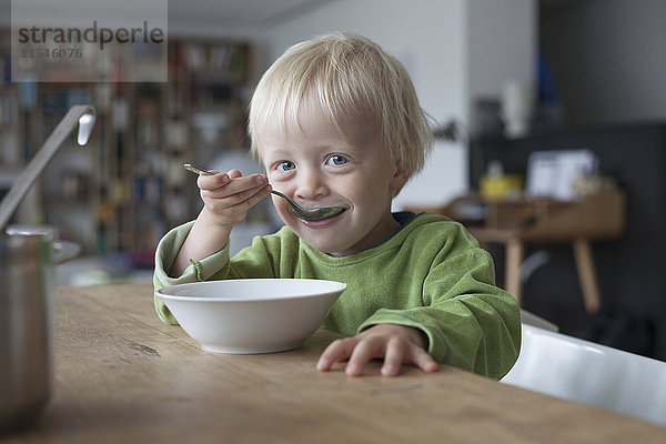 Porträt eines lächelnden kleinen Jungen  der zu Hause Suppe isst.