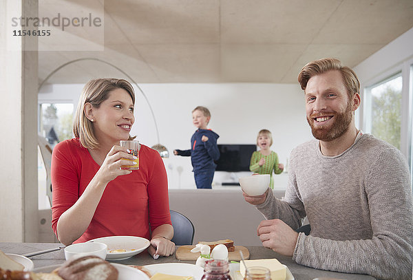 Eltern beim Frühstück zu Hause mit Kindern im Hintergrund