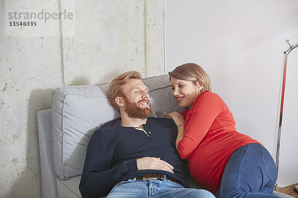 Lächelnder Mann und schwangere Frau auf der Couch liegend