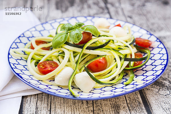 Schale mit Zucchini-Spaghetti mit Mozzarella  Kirschtomaten und Basilikum auf Holz