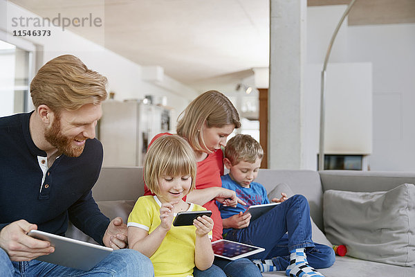Vierköpfige Familie mit mobilen Geräten auf der Couch