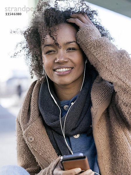 Porträt einer lächelnden jungen Frau  die Musik mit Kopfhörern hört.