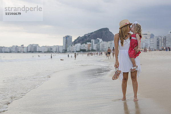 Brasilien  Rio de Janeiro  Mutter trägt und küsst Tochter am Strand von Copacabana