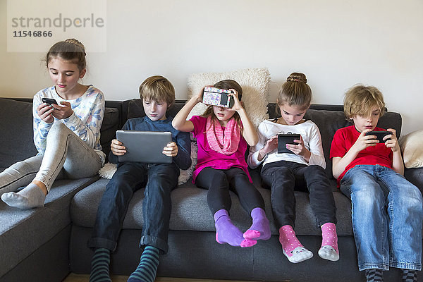 Gruppenbild von fünf Kindern auf einer Couch mit verschiedenen digitalen Geräten