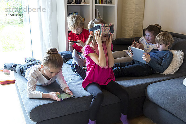 Fünf Kinder auf einer Couch mit verschiedenen digitalen Geräten